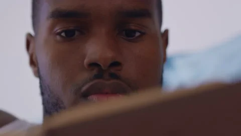 Young man relaxing lying on bed and reading a book in bright modern room. Close Stock Footage 199455229