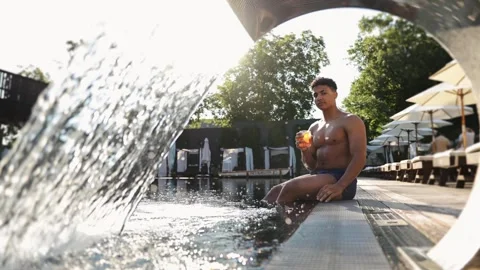 Young man relaxing by the pool with drink, enjoying the warm weather and leisure Stock Footage 333564921