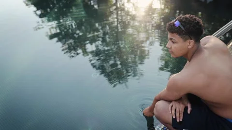 Young man relaxing by pool, touching water, enjoying summer day on vacation Stock Footage 328160139