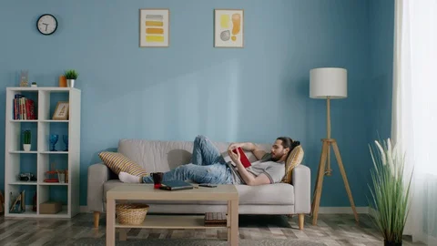 Young Man Is Relaxing on Sofa Vídeo Stock 129886809