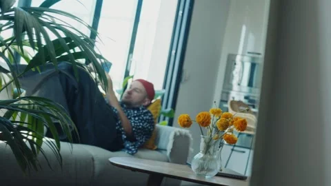 Young man relaxing on sofa using smartphone in modern apartment Stock Footage 312999220