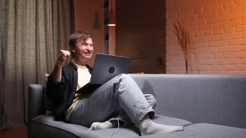 Young man relaxing on a sofa while typing on a laptop, connecting to the 動画素材 347237057