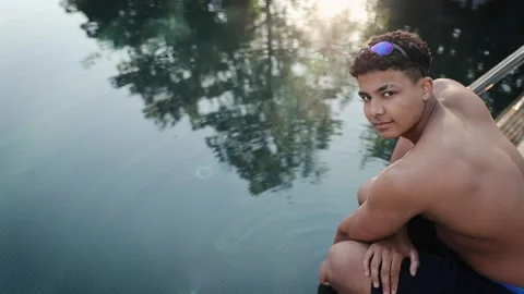 Young man relaxing by swimming pool edge with goggles, enjoying summer holiday Stock Footage 333564914
