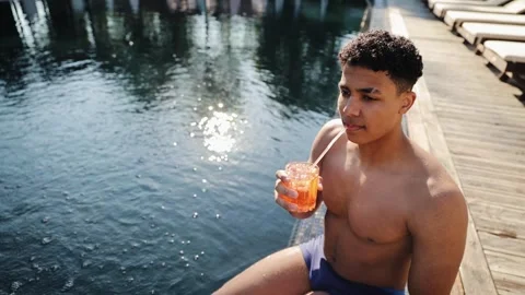 Young man relaxing by swimming pool enjoying vacation with refreshing drink Stock Footage 333564941