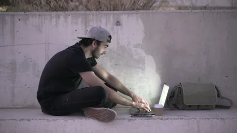 Young man remote working with lap top in public place, sitting in concrete bench Stock Footage 209472231