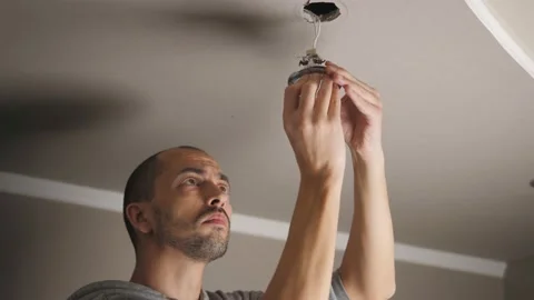 A young man is repairing a ceiling soffit. Replacing the LED lamp at the Vídeo Stock 147651661