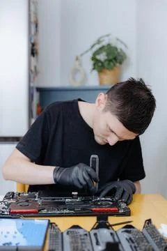 A young man repairs a computer at home. Stock Photos