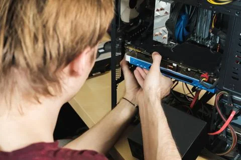 Young man repairs a computer system unit, changes parts, video card and hard Foto stock