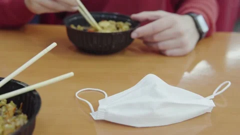A young man in a restaurant eats with chopsticks. A disposable medical face mask Stock Footage 162496789