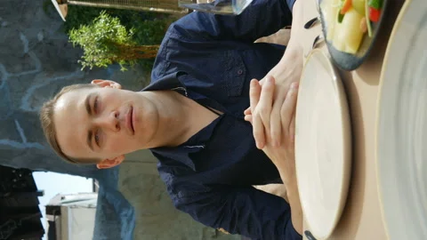 Young man in a restaurant looks at the camera and blinks his eyes.vertical video Stock Footage 136776587