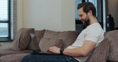 Young man resting on couch at home using laptop talk to family or friend on Stock Footage 269141122