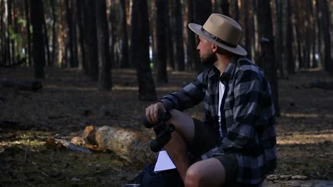 Young man resting on a log and looking through binoculars while hiking Stock Footage 150255651