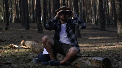Young man resting on a log and looking through binoculars while hiking Stock Footage 150255778