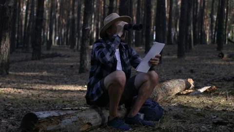 Young man resting, looking through binoculars and checking a map while hiking Stock Footage 150255813