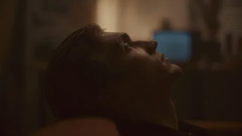 Young Man Resting on Sofa and Gazing Upward Pensively in Dimly Lit Room Stock Footage 307549587