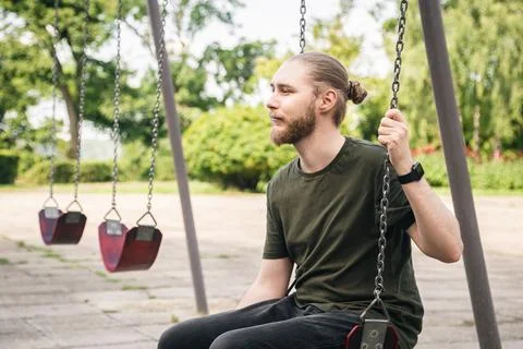 A young man is resting while sitting on a swing in the park. Stock Photos