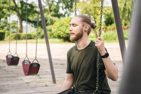 A young man is resting while sitting on a swing in the park. Stock Photos