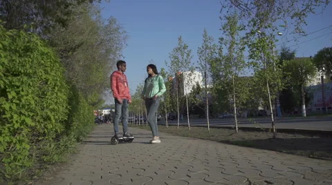 Young man rides on hoverboard for asian girl Stock Footage 63826661