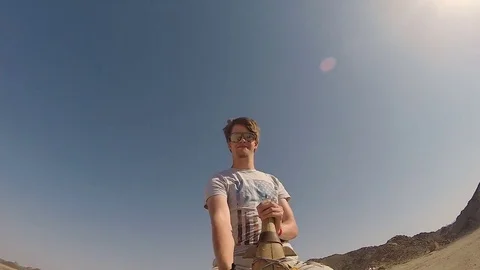 Young man riding on a camel through the desert Vídeo Stock 85057890