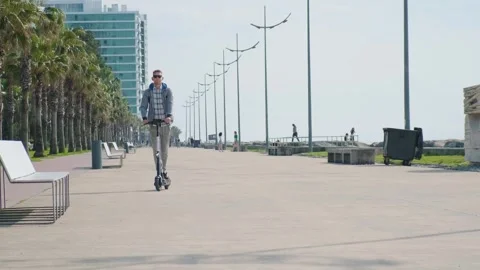 Young man riding electric scooter eco friendly transport along the promenade in Stock Footage 252143997