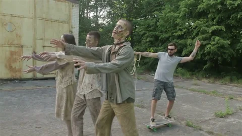 A young man is riding a skateboard using zombies on leashes. Stock Footage 77487393
