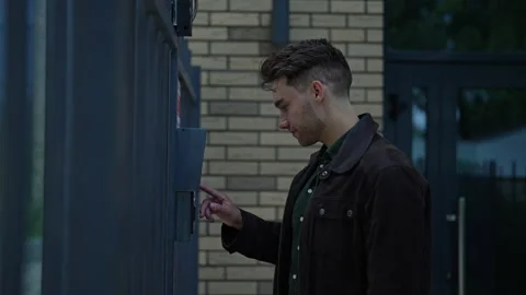 Young man ringing intercom system standing on city street, waiting patiently for Stock Footage 296582926