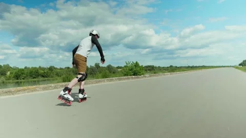 Young man on roller inline skates starting to roll on empty road on a sunny day Stock Footage 132798744