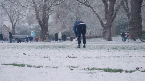 A young man is rolling a big snowball to make a snowman Stock Footage 148118129