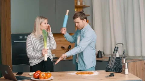 Young man with rolling pin in hand talks to a woman in modern kitchen 스톡 동영상 248523868