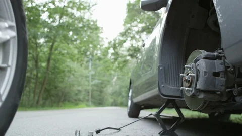Young Man Rolling a Spare Tire From the Back of his Car Stock Footage 79871512