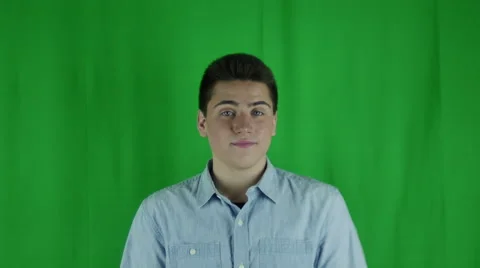 Young man rolls eyes dismissively pulls out phone in front of a greenscreen Stock Footage 59086456