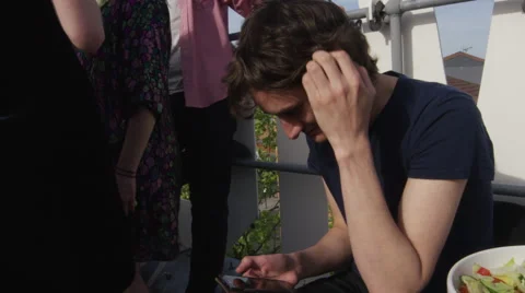 Young man at rooftop party scrolling through messages on mobile phone  Stock Footage 58581846