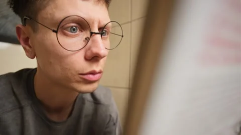 Young man in round glasses moving his eyes side to side while reading Stock Footage 303473960