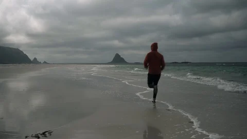 Young man running along the shoreline at the beach Stock Footage