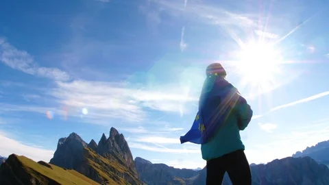 Young man in running clothes standing on mountain peak raising european flag to Stock Footage 122102070