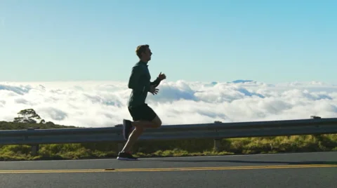 Young Man Running on Mountain Road at Sunset Above the Clouds. Slow Motion HD Stock Footage 59820515