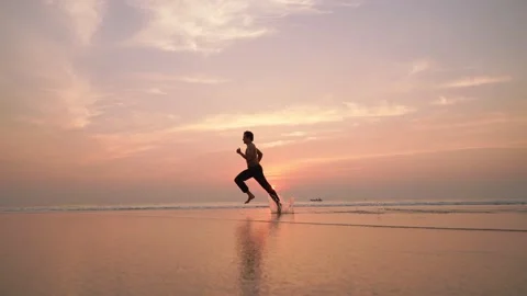 A young man running or sprinting on the beach against the rising sun. Stock Footage 145923308
