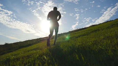 Young man running over green hill over blue sky background. Slow motion Stock Footage
