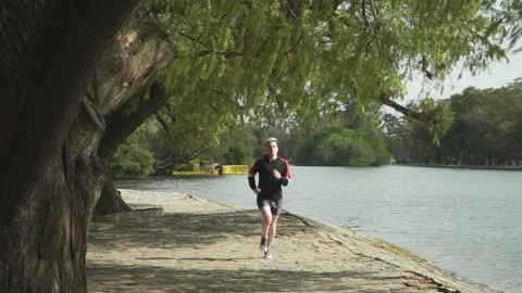 A young man running on a pathway beside lake towards camera Stock-Footage 140551085