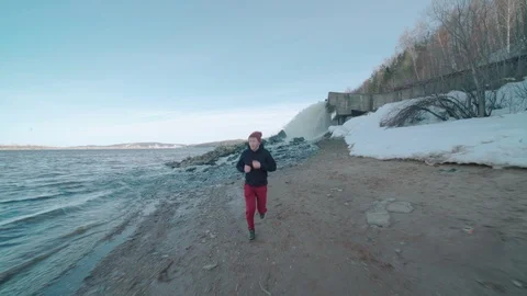 Young man running on river coast with waterfall behind Stock Footage 106441828