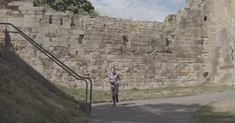 Young man is running towards the camera from the castle wall at Tonbridge Castle Stock Footage 136761261