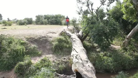 Young Man Runs Over Fallen Log Above African Stream Stock Footage 10721477