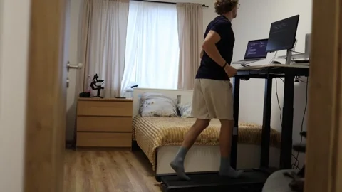 Young man runs on treadmill while working online at computer in home office Stock-Footage 347269923