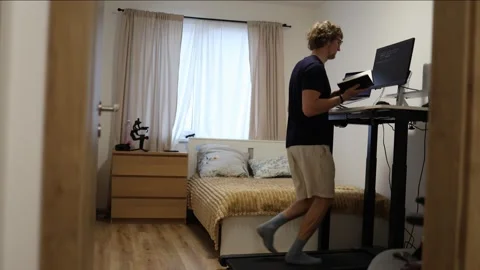 Young man runs on treadmill while studying programming at home office Stock-Footage 347269964