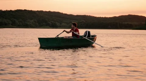 Young man sailing boat on the river and fishing, sunset Stock Footage 66284935