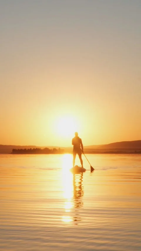 A young man is sailing through a quiet place on a SUP board at sunset. Stock Footage 267647082