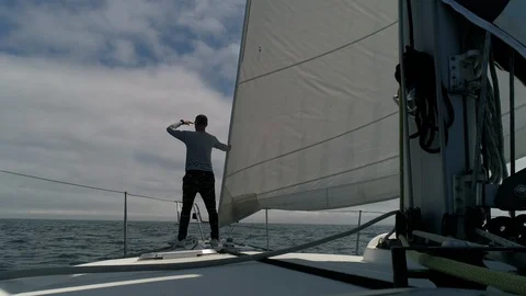 A young man sailor on the deck of a sailing yacht in the ocean looks to skyline  Vídeo Stock 114814414