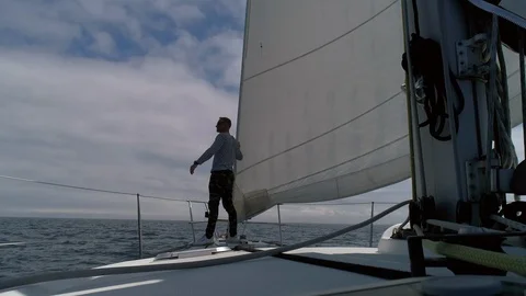 A young man sailor on the deck of a sailing yacht in the ocean looks to horizon Stock Footage 114816462