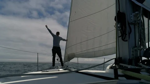 A young man sailor on the deck of a sailing yacht looks forward raising his hand Stock Footage 114817036