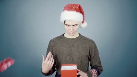 Young man in Santa hat opening a gift box with a surprise pulls out long Video stock 70223226